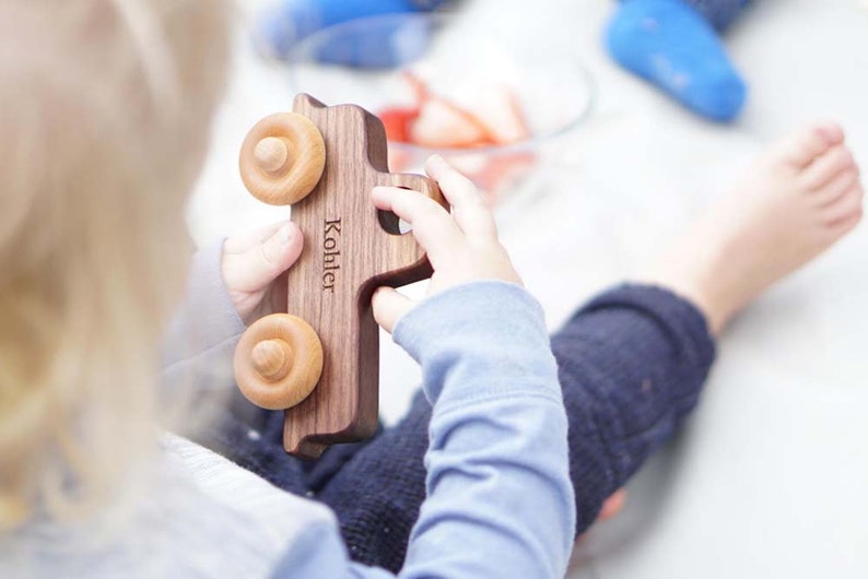 K&ouml;nnte beinhalten: Ein Kind h&auml;lt ein h&ouml;lzernes Spielzeugauto mit dem Namen "Kohler" auf der Seite. Der LKW hat zwei Holzr&auml;der und ist aus dunklem Holz.
