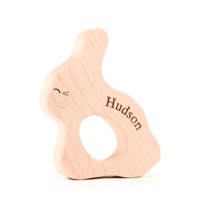May include: A light wood bunny-shaped teether with a hole in the middle and the name "Hudson" engraved on the side.