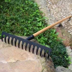 May include: A garden rake featuring a long, smooth, light-colored wooden handle attached to a wide, black metal head with fourteen evenly spaced, curved tines. The tool is designed for gathering leaves or leveling soil in outdoor garden spaces.