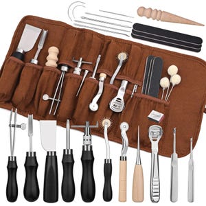 May include: A brown leather tool roll filled with various leathercraft tools. The set includes a variety of knives, needles, edge bevelers, and other specialized tools with wooden and black handles. The tools are designed for leatherworking.
