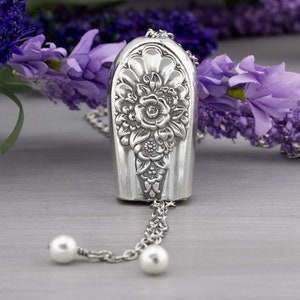 May include: A silver necklace with a floral design pendant and two pearl accents. The pendant is shaped like a teardrop and features a detailed floral pattern.
