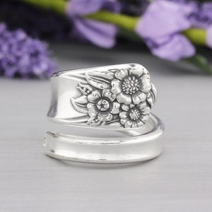 May include: A silver spoon ring with a floral design. The ring is made from a spoon that has been bent and shaped to form a ring. The floral design is on the spoon's head. The ring is a unique piece of jewelry.