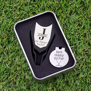 Golf ball marker and divot tool set in a gift tin box. Divot tool has marker engraved with a large letter J with name in the center, our forever and the date below the large letter. The round marker comes with a hat clip and is engraved best hubby by par with crossed clubs graphic.