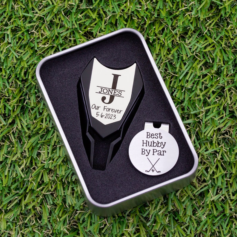 Golf ball marker and divot tool set in a gift tin box. Divot tool has marker engraved with a large letter J with name in the center, our forever and the date below the large letter. The round marker comes with a hat clip and is engraved best hubby by par with crossed clubs graphic.