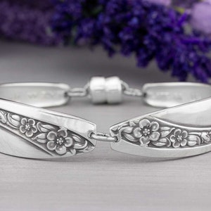 May include: A silver bracelet made from a repurposed vintage spoon with a floral design. The bracelet is open and has a magnetic clasp.