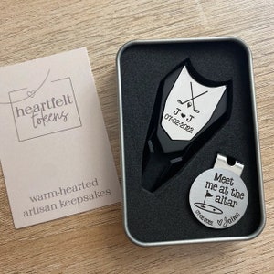 Golf ball marker and divot tool set in a gift tin box. Divot tool has marker engraved with crossed clubs with an initial on each side. The round marker comes with a hat clip and is engraved Meet me at the altar with the date, golf green graphic and a heart with name at the bottom.