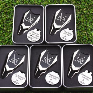 This image shows an order for 5 custom divot tin sets for a wedding party. Silver and black divot tools with initials with crossed clubs. The round markers are engraved for the groom, best man and groomsmen.