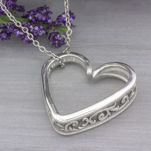 May include: A silver heart-shaped pendant necklace with a delicate chain and intricate scrollwork design.