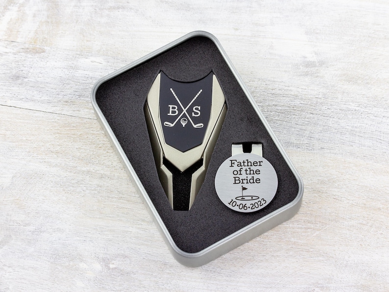 beige color metal divot tool with black metal divot tool ball marker personalized with crossed clubs with initials on each side. Silver stainless steel golf marker engraved father of the bride with golf flag graphic and date.