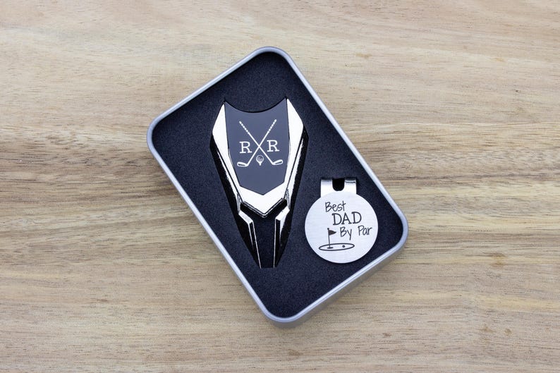 silver color metal divot tool with black metal divot tool ball marker personalized with crossed clubs with initials on each side. Silver stainless steel golf marker engraved best dad by par with golf flag graphic.