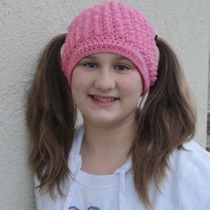 May include: A pink crocheted hat with two pigtails. The hat has a ribbed texture and covers the ears.