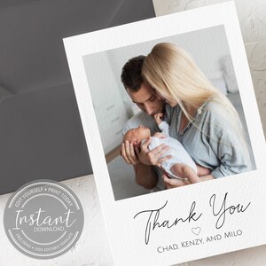 May include: White thank you card with a photo of a couple holding a newborn baby. The card features the words "Thank You" in elegant script, with the names "Chad, Kenzy, and Milo" below. A gray envelope is visible in the background.