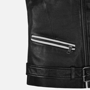May include: Close-up of a black leather jacket with a silver zipper and a white stripe detail on the pocket. The jacket has a belt with a silver buckle at the waist. The leather appears smooth and the stitching is precise.