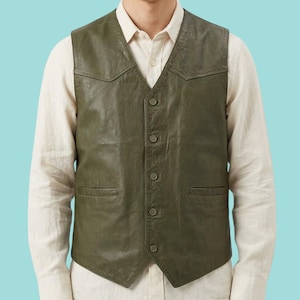 May include: Olive green leather vest with a V-neck and button-up closure. The vest has two front pockets and a classic design. The model is wearing a light-colored button-down shirt underneath the vest.