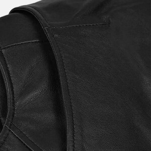 May include: Close-up of a black leather jacket, showcasing the texture and stitching details. The image highlights the shoulder and upper chest area, emphasizing the quality of the material and craftsmanship. The jacket appears to be a classic style.