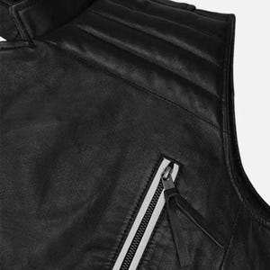 May include: Close-up of a black leather vest with a high collar and quilted shoulder detailing. The vest features a diagonal zipper with a white stripe and a black leather pull.