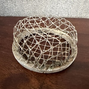 May include: A vintage, round, metal flower frog with a cage-like design. The flower arranging tool has a circular base and a webbed top, perfect for holding flower stems in place. The metal has a weathered, aged appearance, suggesting it is antique.