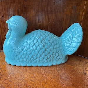 Op de afbeelding: Een turquoise keramieken kalkoenbeeldje met een gedetailleerd gevormd verenpatroon over het lichaam, een gladde kop met een gedefinieerde snavel en lellen, en een uitgewaaierde staart. Het object heeft een glanzende afwerking en rust op de ondergrond.