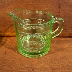 Peut inclure: Un verre doseur en verre vert clair transparent avec une anse et un bec verseur. L'extérieur présente des graduations en relief indiquant les mesures en tasses et en onces, avec le texte ONE CUP, 8 OZ, 3/4 CUP, 6 OZ, 1/2 CUP, 4 OZ et 1/4 CUP, 2 OZ.