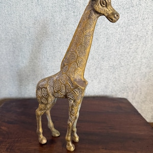 Op de afbeelding: Een messing girafbeeldje met een getextureerd, patroonlichaam. De giraf staat op vier poten, met een lange nek en kleine oren. Het beeldje is goudkleurig en lijkt van metaal te zijn.