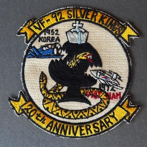 May include: Embroidered patch with the text "VF-92 SILVER KINGS" and "20th ANNIVERSARY". The patch features a black bird, a snake, and two airplanes, with the words "KOREA" and "VIETNAM".
