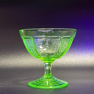 Può includere: Una vivace coppetta da dessert in vetro verde con base a piedistallo. La ciotola presenta un motivo decorativo sul bordo e sui lati. La base ha un motivo a diamante. Il vetro ha una leggera lucentezza.