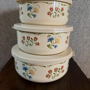 Puede incluir: Tres cuencos apilables de color crema con tapas. Cada cuenco presenta un diseño floral con flores rojas, azules y amarillas. Las tapas son del mismo color crema que los cuencos. Ideales para la cocina y el almacenamiento.