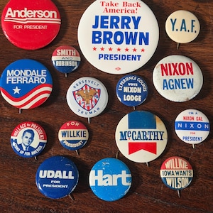 May include: A collection of fourteen circular political campaign buttons featuring various candidates and slogans including Anderson, Jerry Brown, Y.A.F., Mondale Ferraro, Smith and Robinson, Roosevelt Truman, Nixon Lodge, Nixon Agnew, Wallace, Willkie, McCarthy, Nixon, Udall, Hart, and Willkie Iowa Wants Wilson.