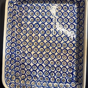 May include: Rectangular ceramic baking dish with a blue and white pattern. The pattern features concentric circles in shades of blue, brown, and white. The dish has a white rim and is suitable for baking or serving food.