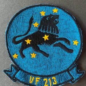 May include: Embroidered patch with a black lion and yellow stars on a blue background. The patch is circular with a banner at the bottom, displaying the text "VF 213" in yellow.
