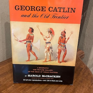 May include: A hardcover book titled "GEORGE CATLIN and the Old Frontier" with an orange and black cover. The cover features illustrations of Native American figures and text that reads "A Biography and Picture Gallery of the Dean of Indian Painters".