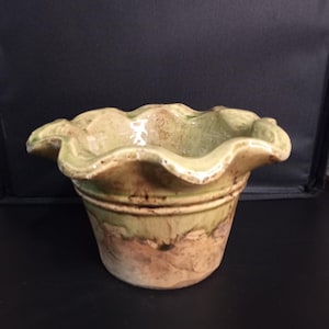May include: A ceramic planter with a ruffled, wavy rim. The upper portion features a glossy, light green glaze, while the lower section transitions into a textured, earthy brown, unglazed terracotta finish with visible dark brown speckling.