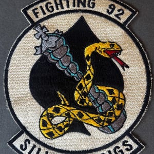 Op de afbeelding: Geborduurde patch met een gele slang en rode tong gewikkeld rond een zwarte schoppen. De patch heeft de tekst "FIGHTING 92" bovenaan en "SILVER KINGS" onderaan, in witte letters, op een beige achtergrond.