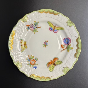 May include: White ceramic plate with a scalloped green and gold rim. The plate is decorated with colorful butterflies and floral designs. The butterflies have yellow, orange, and pink wings. The flowers are blue, orange, and purple.
