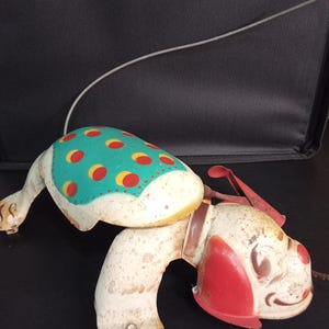 Gioco da tirare e correre a forma di cucciolo Mobo in latta, anni '50. La leva non è funzionante e necessita di nuove ruote. Dimensioni: 30,5 cm di lunghezza x 20,3 cm di larghezza.