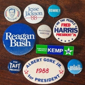 May include: A collection of ten vintage political campaign buttons and one rectangular pin. The items feature various names and slogans including Rockefeller, Jesse Jackson '88, Romney, Reagan Bush, McGovern Shriver, Fred Harris, Kemp '96, Taft, Albert Gore Jr. 1988, and Udall.