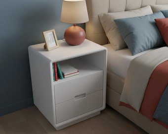 Puede incluir: Una mesita de noche blanca con marco redondeado, que cuenta con un estante de almacenamiento abierto con tres libros y un cajón inferior con tirador empotrado. Una lámpara de mesa color terracota con pantalla beige y un marco de fotos de madera.