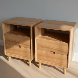 May include: Two matching wooden nightstands. Each nightstand has a drawer and an open shelf. The nightstands are made of light-colored wood and have rounded corners. The nightstands are supported by short, tapered legs.