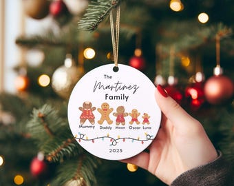 May include: A white, round Christmas ornament with a gold string, held in a hand. The ornament features the text "The Martinez Family" and gingerbread people representing family members. The year 2025 is printed at the bottom.
