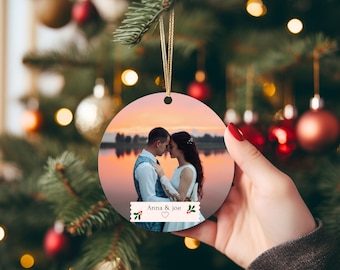 Könnte beinhalten: Runder Weihnachtsschmuck mit einem Foto eines Paares bei Sonnenuntergang. Der Schmuck hat einen goldenen Aufhänger und den Text "Anna & Joe". Eine festliche Dekoration für den Weihnachtsbaum.