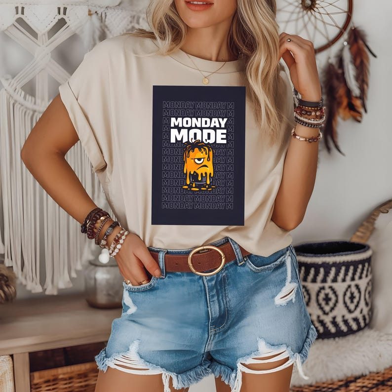 Pu&ograve; includere: T-shirt beige con la scritta "MONDAY MODE" e un disegno di un volto giallo che si scioglie. La maglietta &egrave; abbinata a pantaloncini di jeans e una cintura marrone. L'immagine &egrave; di una persona.