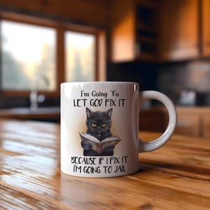 Puede incluir: Taza de cerámica blanca con una ilustración de un gato negro leyendo un libro y el texto "I'm Going To LET GOD FIX IT BECAUSE IF I FIX IT I'M GOING TO JAIL". La taza tiene un asa curva.