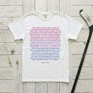 May include: White t-shirt with Russian text and the phrase "Okay, I'm done." A hockey stick and a necklace with a cross are on the side. The shirt's text is in a handwritten style.