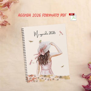 Puede incluir: Agenda con espiral con el texto "Mi agenda 2026" y "AGENDA 2026 FORMATO PDF". La portada presenta una ilustración en acuarela de una persona con sombrero y vestido, con detalles de libélulas. La agenda es de color crema.