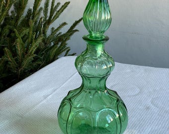 Peut inclure: Une bouteille décorative en verre vert avec un bouchon pointu. La bouteille a une base bulbeuse et un design détaillé. Le bouchon est d'une nuance de vert plus foncée. La bouteille est sur une surface blanche.