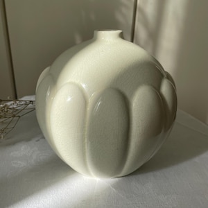 Op de afbeelding: Een lichtgroene keramische vaas met een ronde body en een smalle hals. De vaas heeft een textuur met verticale, afgeronde ribbels. De vaas staat op een wit oppervlak.