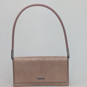 May include: A rectangular shoulder bag in a dusty rose colour with a textured snakeskin pattern. The bag features a single, smooth, arched handle in a matching rose tone, attached with dark metallic hardware, and a small silver-toned metal bar.