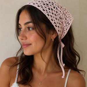 May include: A light pink crochet headscarf featuring an openwork diamond pattern and long, thin ties at the back. The triangular-shaped accessory is crafted from yarn and is designed to be worn tied securely around the head.