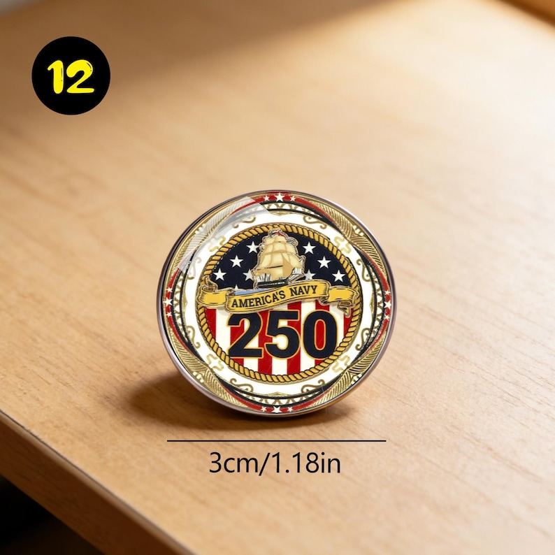 May include: A round commemorative coin with a nautical theme, featuring a sailing ship, stars, and the text "AMERICA'S NAVY 250". The coin is approximately 1.18 inches (3cm) in diameter and has a gold and red border. A yellow circle with the number 12 is in the upper left corner.