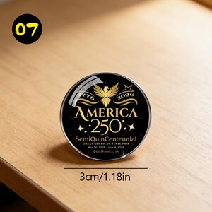 May include: A round, black button with gold text and a gold eagle design. The text reads "AMERICA 250" with the years "1776" and "2026". The button is 1.18 inches in diameter and commemorates the SemiQuinCentennial.